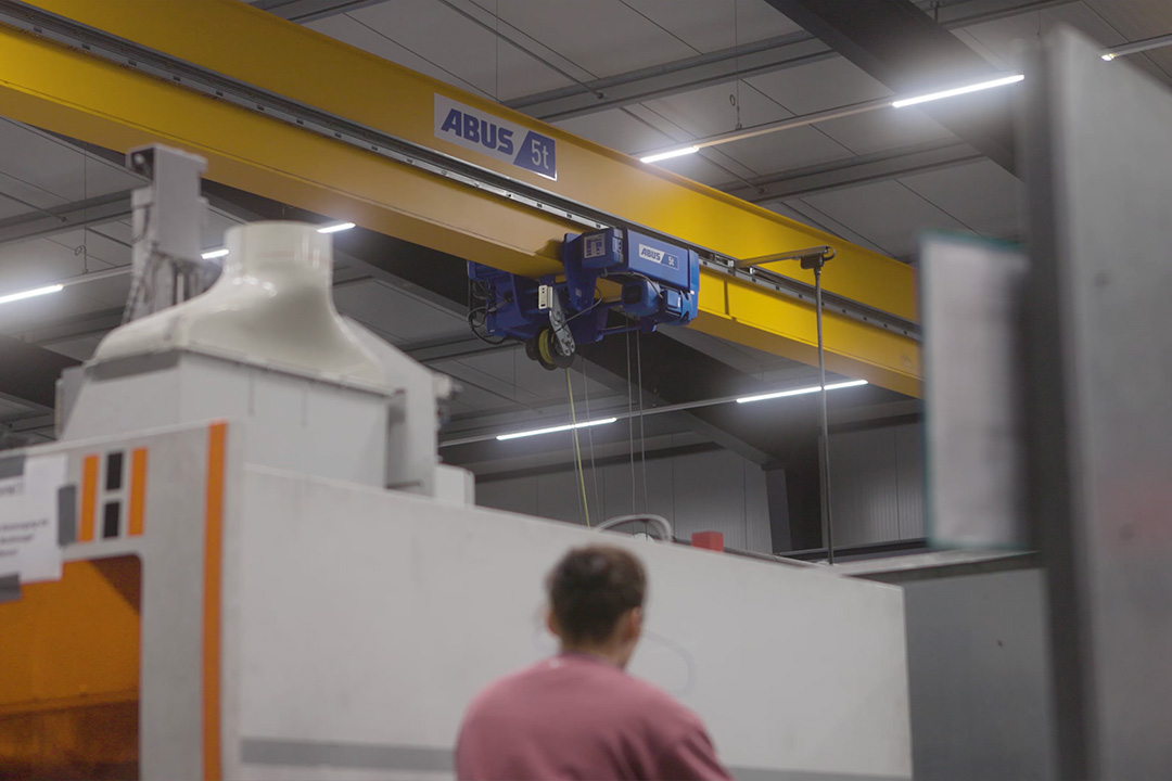 Ein Kran an der Decke, im Vordergrund verschwommen eine Arbeiterin.