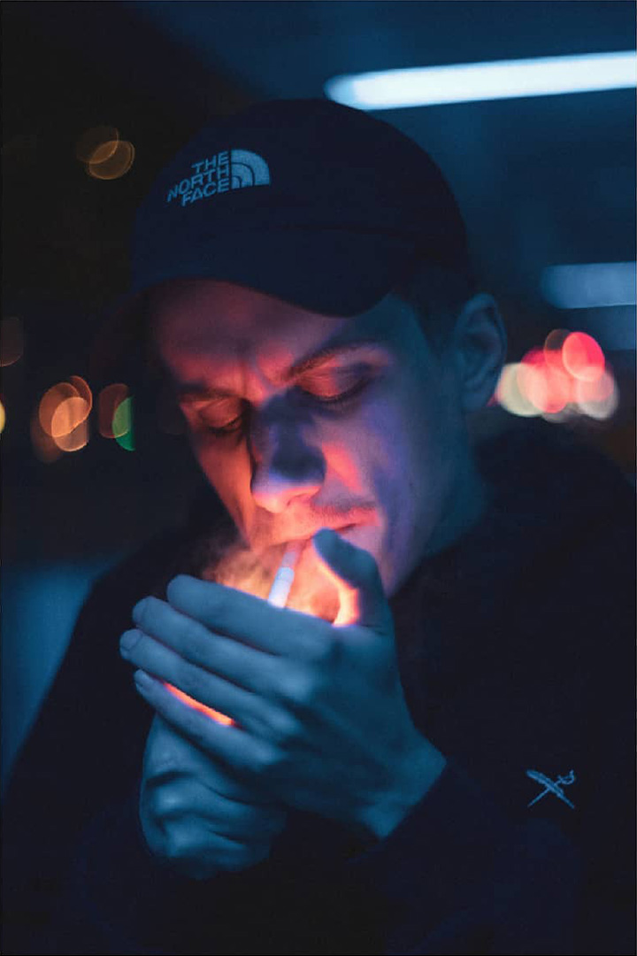 Ein Mann in blauem Licht, der sich eine Zigarette anzündet mit einer warmen Flamme.