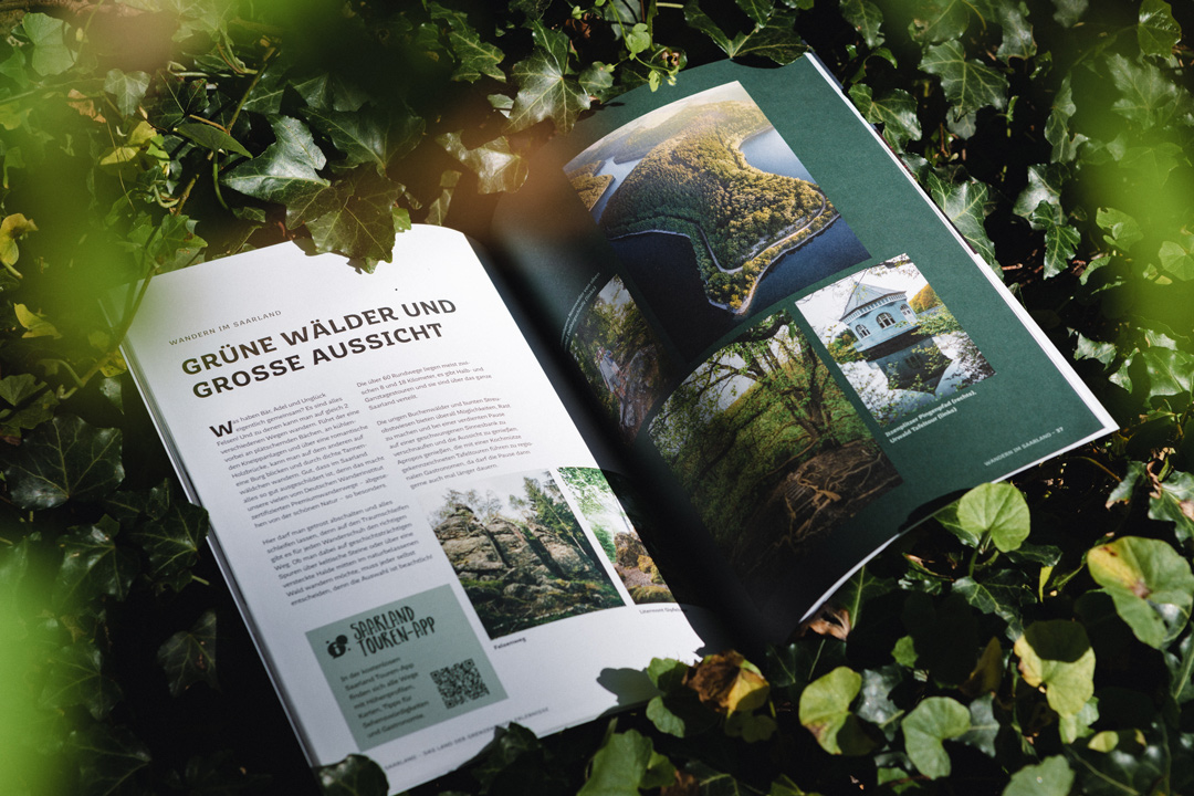 Bild des Heimat Magazins der Tourismus Zentrale Saarland, welches an einen Baumstamm im Wald lehnt. Es zeigt 2 Innenseiten.