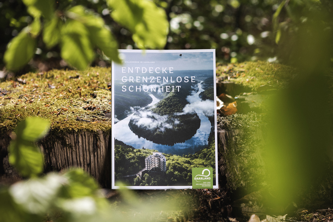 Bild des Heimat Magazins der Tourismus Zentrale Saarland, welches an einen Baumstamm im Wald lehnt.